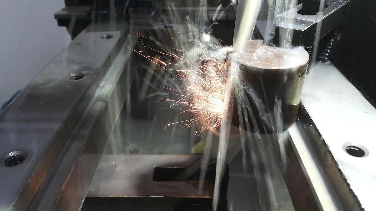 Hilo de electroerosión cortando una pieza de acero entre chispas y refrigerante